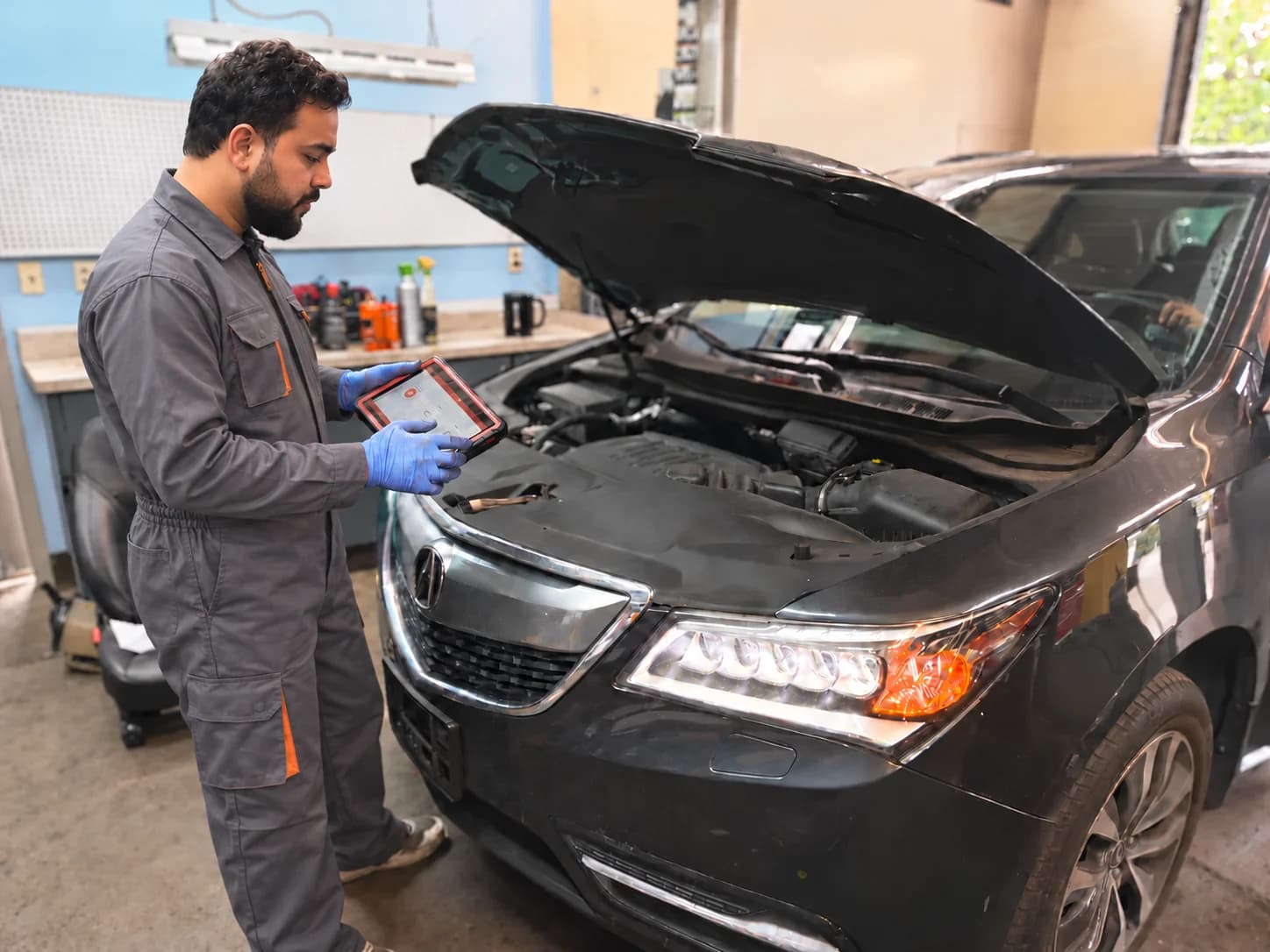 Technician using a diagnostic tablet beside an Acura engine bay